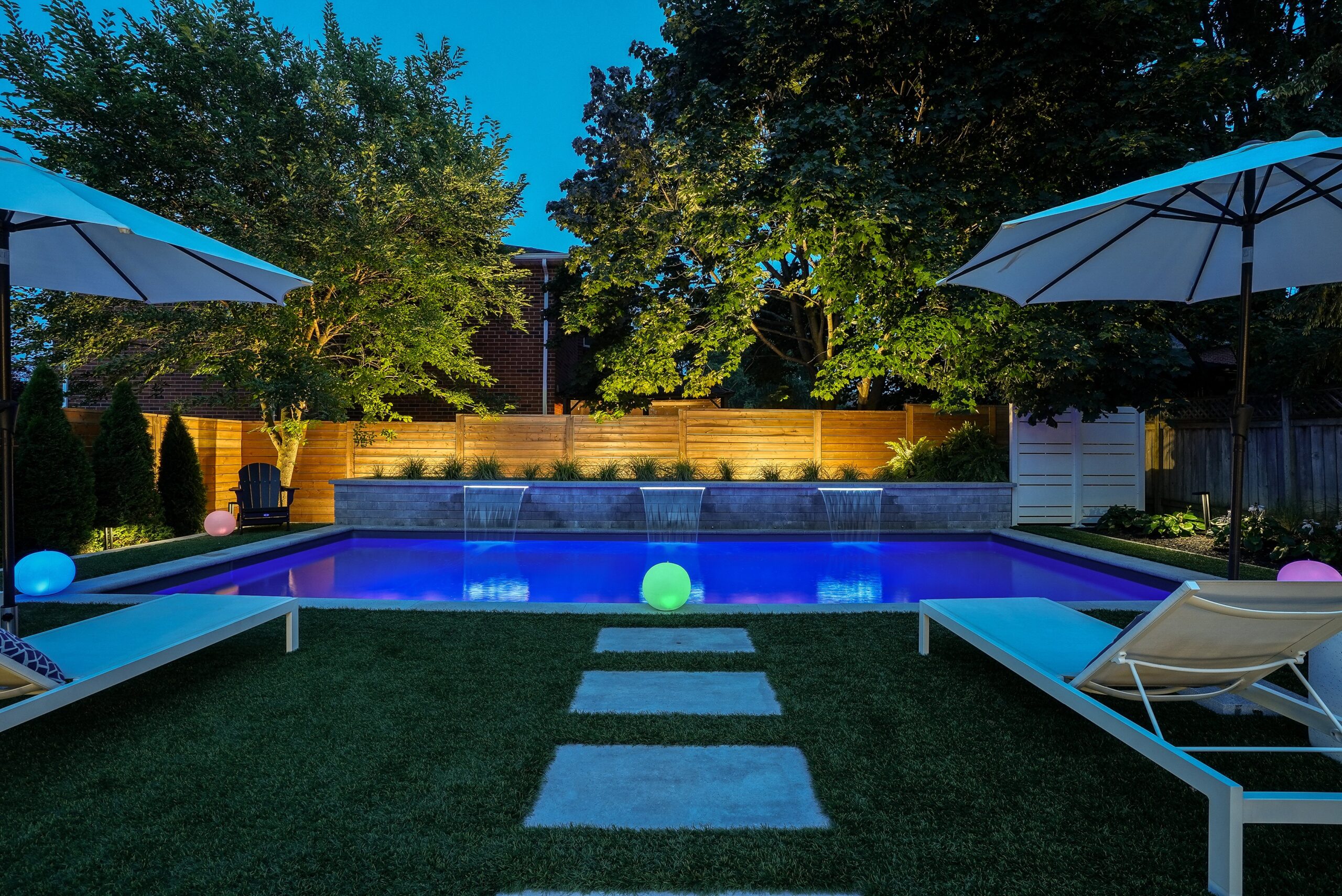 Twilight photo of pool with water features and lit landscaping in Cambridge